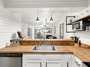 A modern kitchen with a wooden countertop, stainless steel sink, white cabinets, and pendant lighting. - Turkey Nest by Beyond Expectations- Renovated 2BR (Gatlinburg)