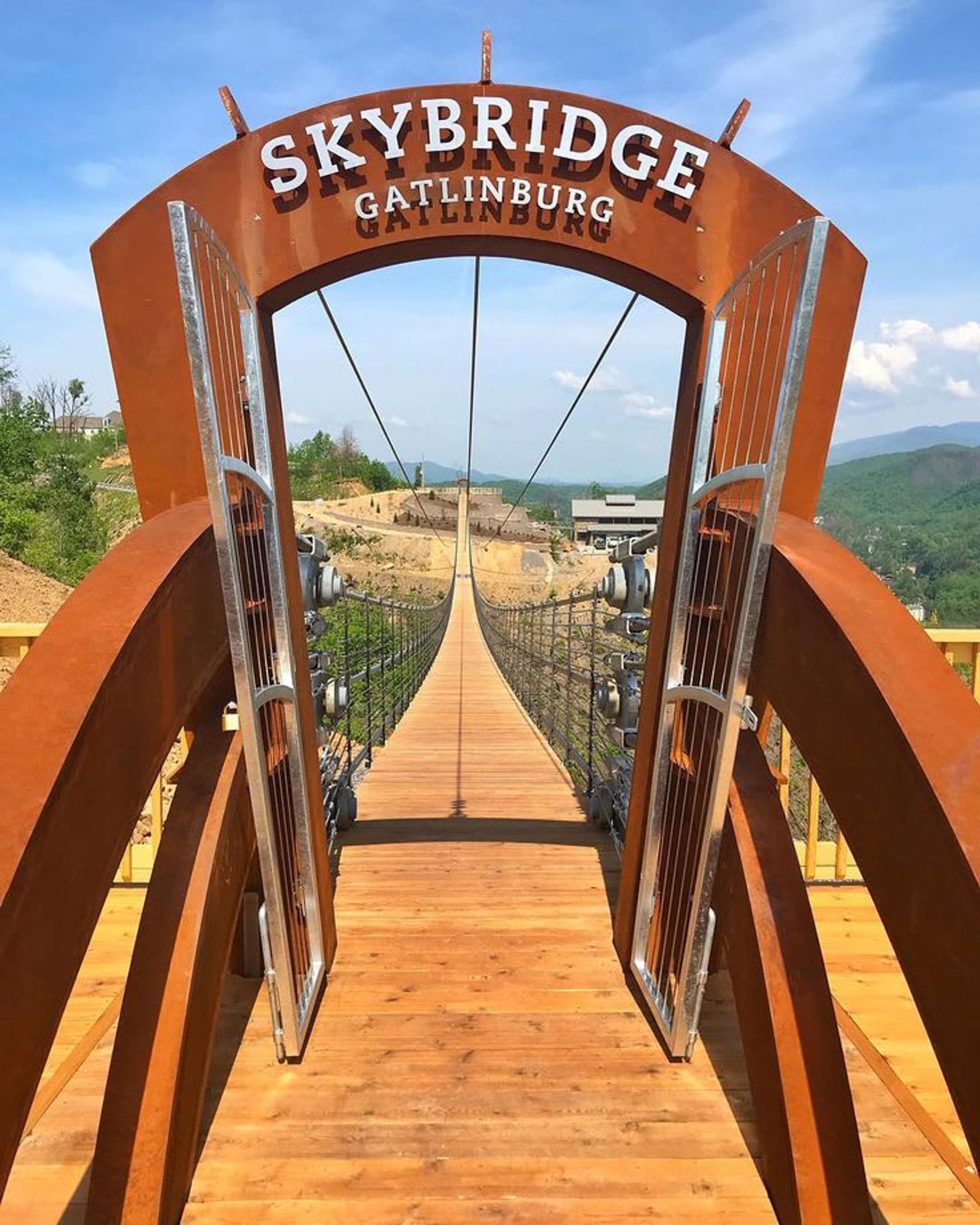 A wooden walkway leading to a metal archway with 'Skybridge Gatlinburg' written on it.