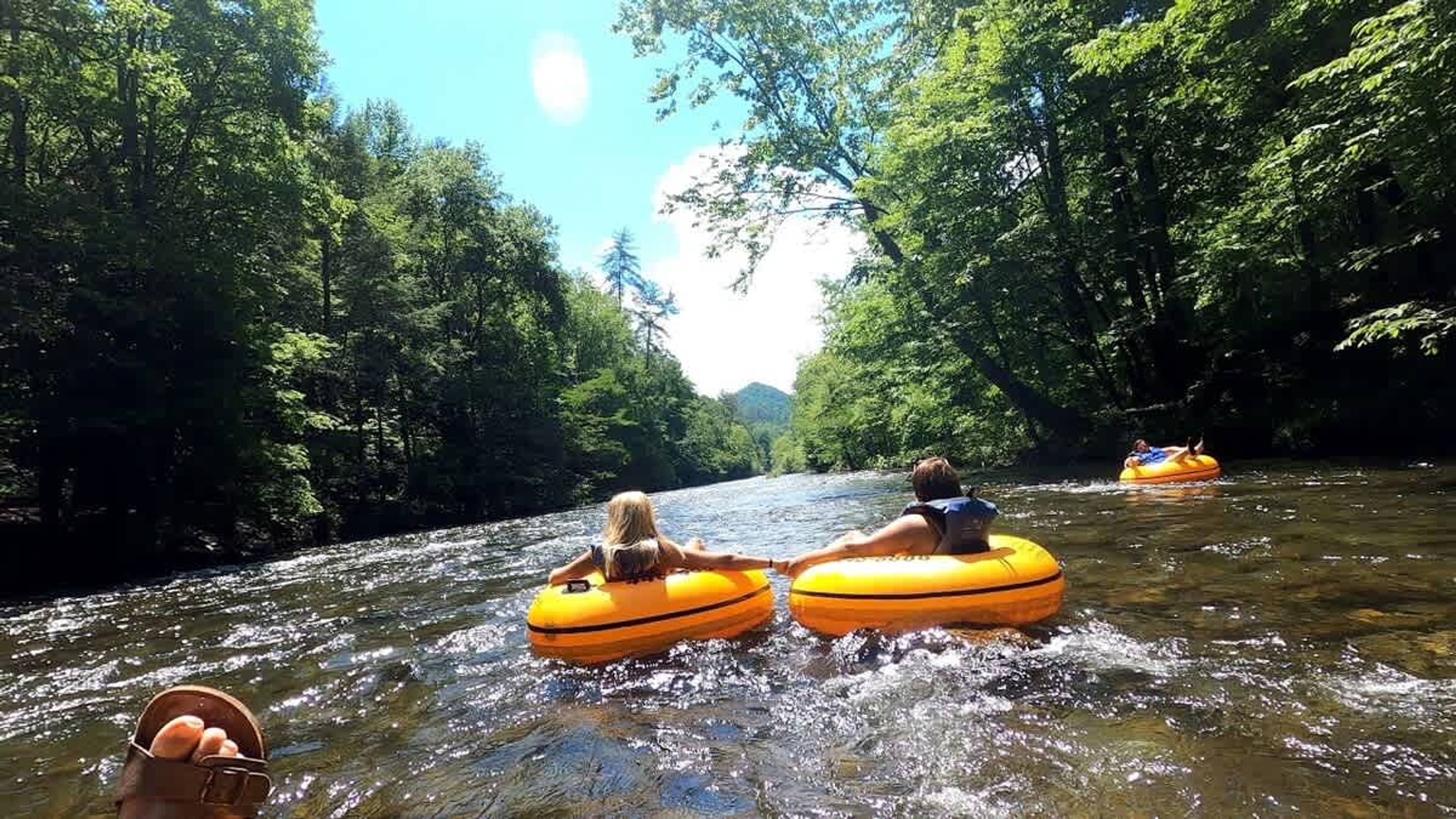People floating on yellow tubes in a river surrounded by trees.