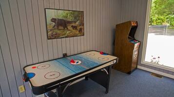 Una mesa de billar con un cuadro de un oso encima y una máquina de pinball a la derecha.