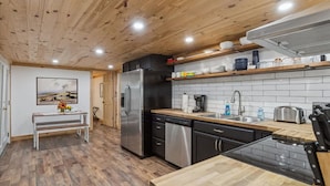 Una cocina moderna con suelo de madera, un refrigerador de acero inoxidable, un lavavajillas y un banco de madera.