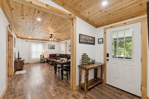 A wooden-floored living area with a sofa, dining table, and a door with a window. - Creekside Retreat by Beyond Expectations (Pigeon Forge)