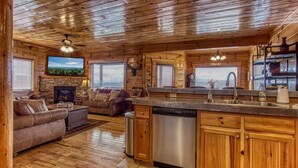A log cabin interior with a living room, fireplace, kitchen, and wooden ceiling. - Majestic Overlook II by Beyond Expectations (Sevierville)