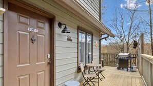 Eine Holzdar Terrasse mit Grill, eine Tür mit Rauchverbot-Hinweis und ein kleiner Tisch mit Stühlen.