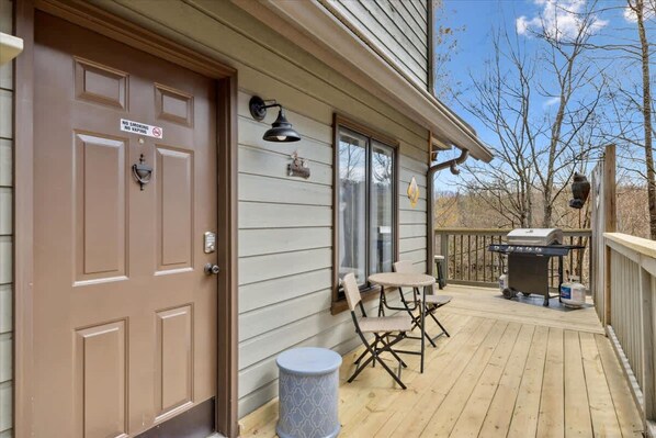 A wooden deck with a grill, a door with a no-smoking sign, and a small table with chairs. - Bear Valley Cabin by Beyond Expectations (Pigeon Forge)