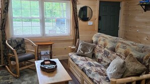 L’intérieur d’un chalet accueillant, avec un plafond en bois, un canapé agrémenté de coussins à motifs, un fauteuil à bascule, une petite table avec un plateau et une fenêtre avec des rideaux.