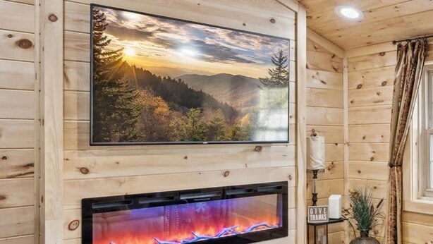 L’intérieur d’un chalet en bois, avec une cheminée, une photographie de paysage encadrée et un luminaire au plafond.