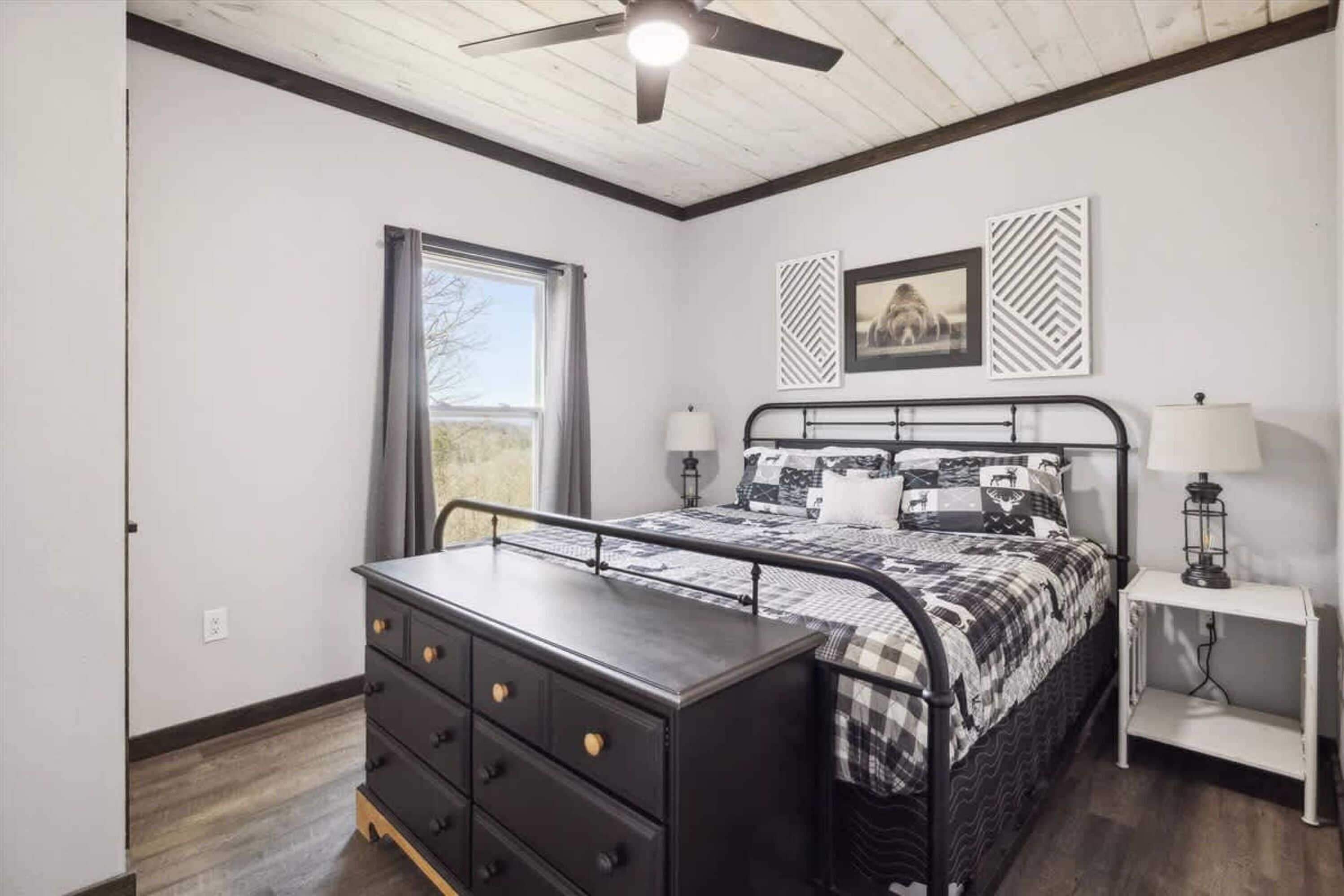 A bedroom with a bed, dresser, nightstand, ceiling fan, window, and wall decor.