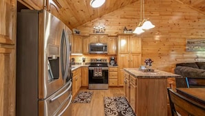 A wooden interior with a kitchen featuring stainless steel appliances, wooden cabinets, and a central island. - Magic Mountain Cabin by Beyond Expectations With Views (Sevierville)