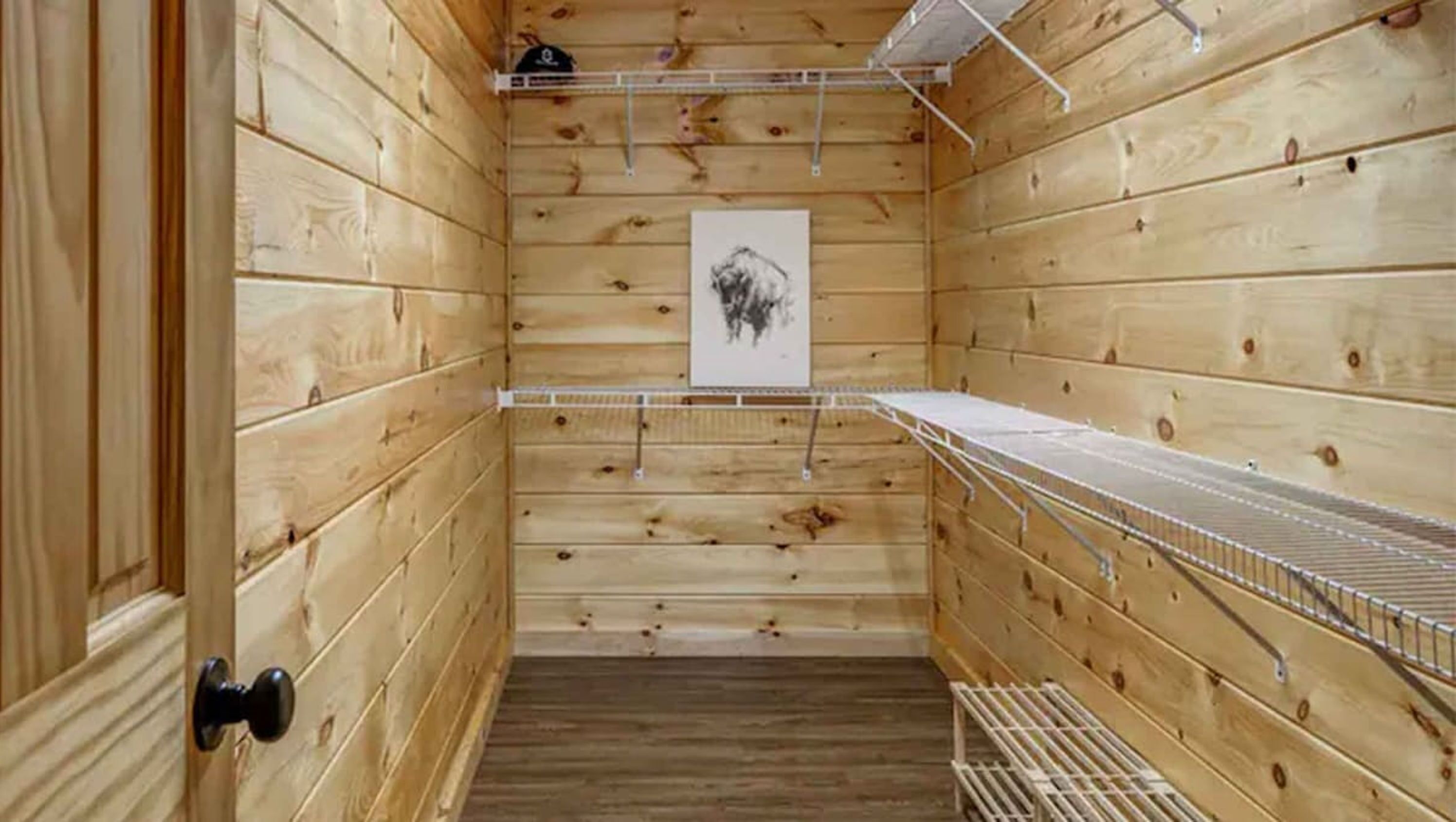 Un intérieur en bois avec une porte, une étagère en métal et un tableau encadré accroché au mur.