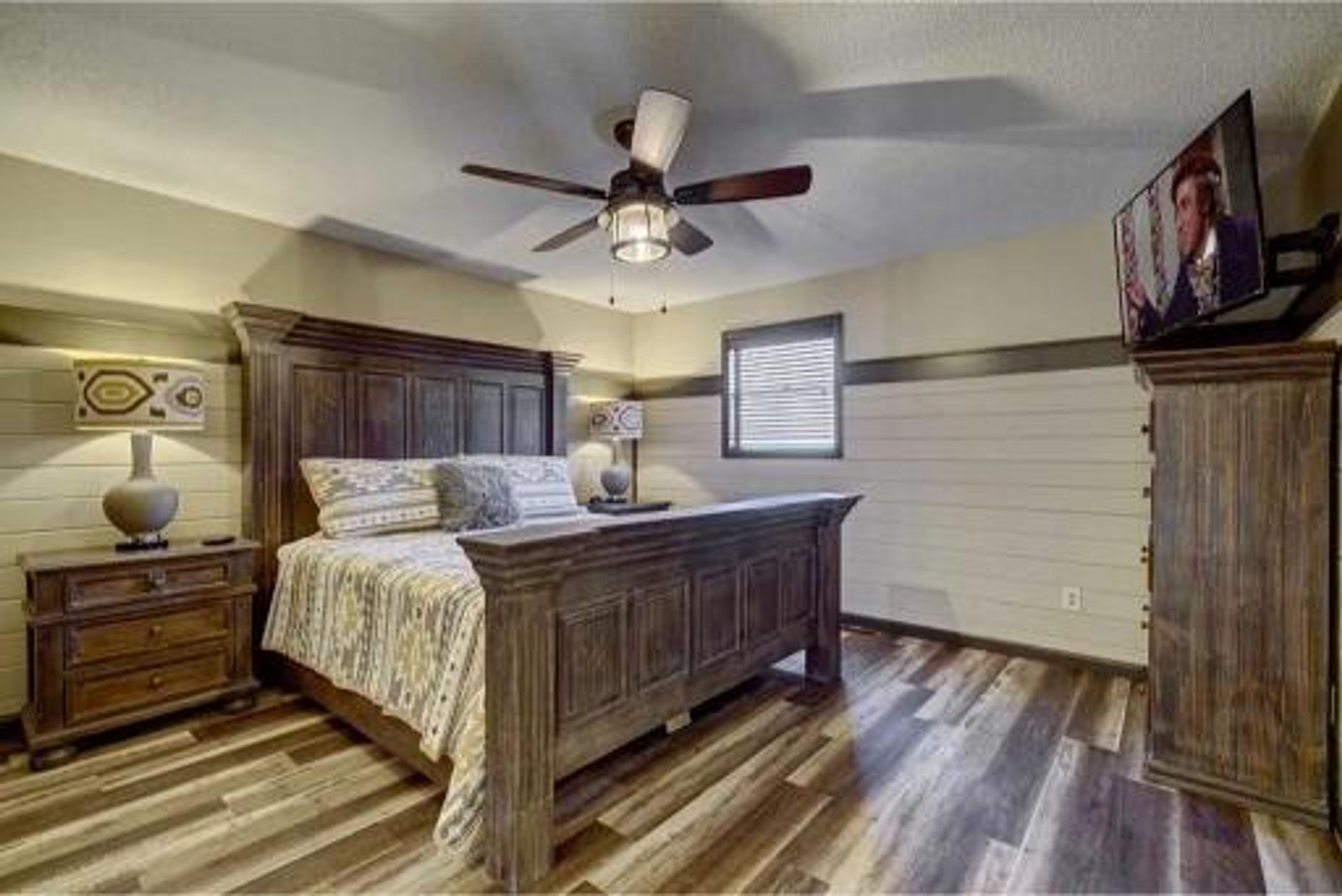 A bedroom with a wooden bed, a ceiling fan, a nightstand, and a dresser.