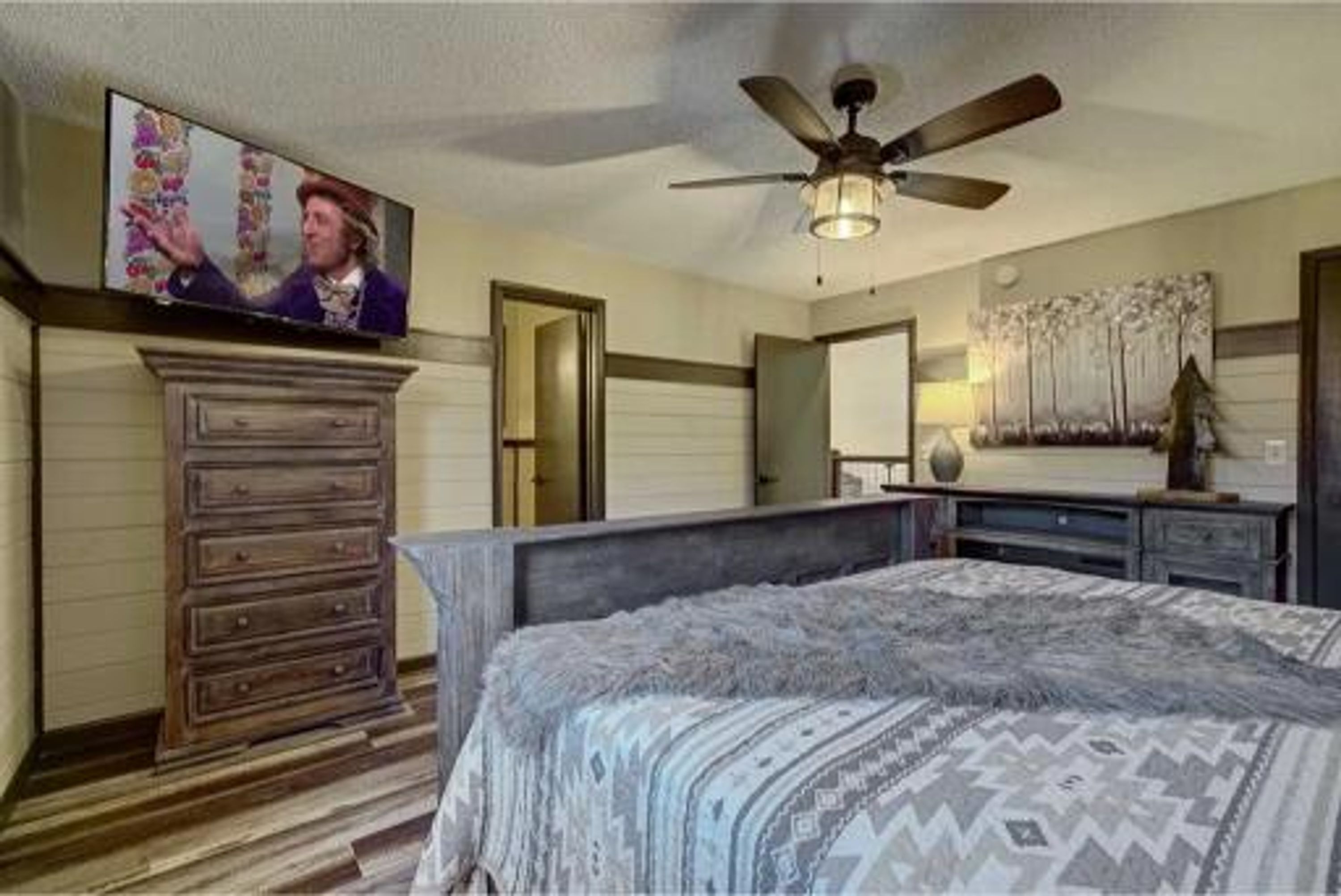 A bedroom with a bed, a dresser, a television, and a ceiling fan.