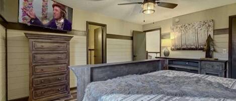 A bedroom with a bed, a dresser, a television, and a ceiling fan.