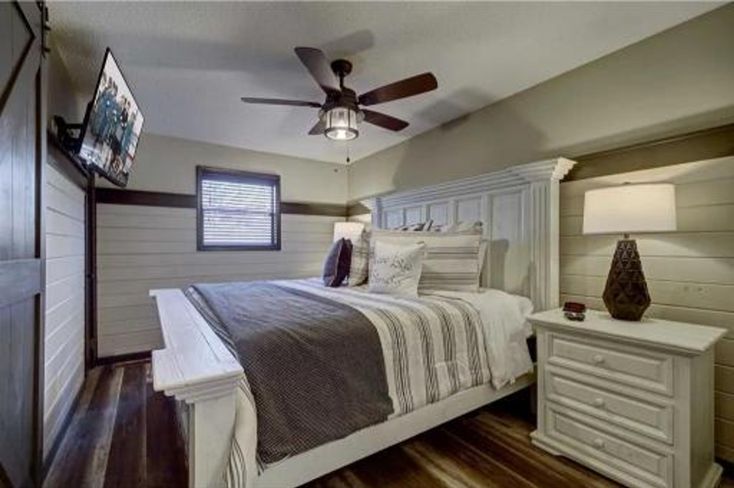 A bedroom with a bed, a nightstand, a ceiling fan, a window, and a wall-mounted picture.