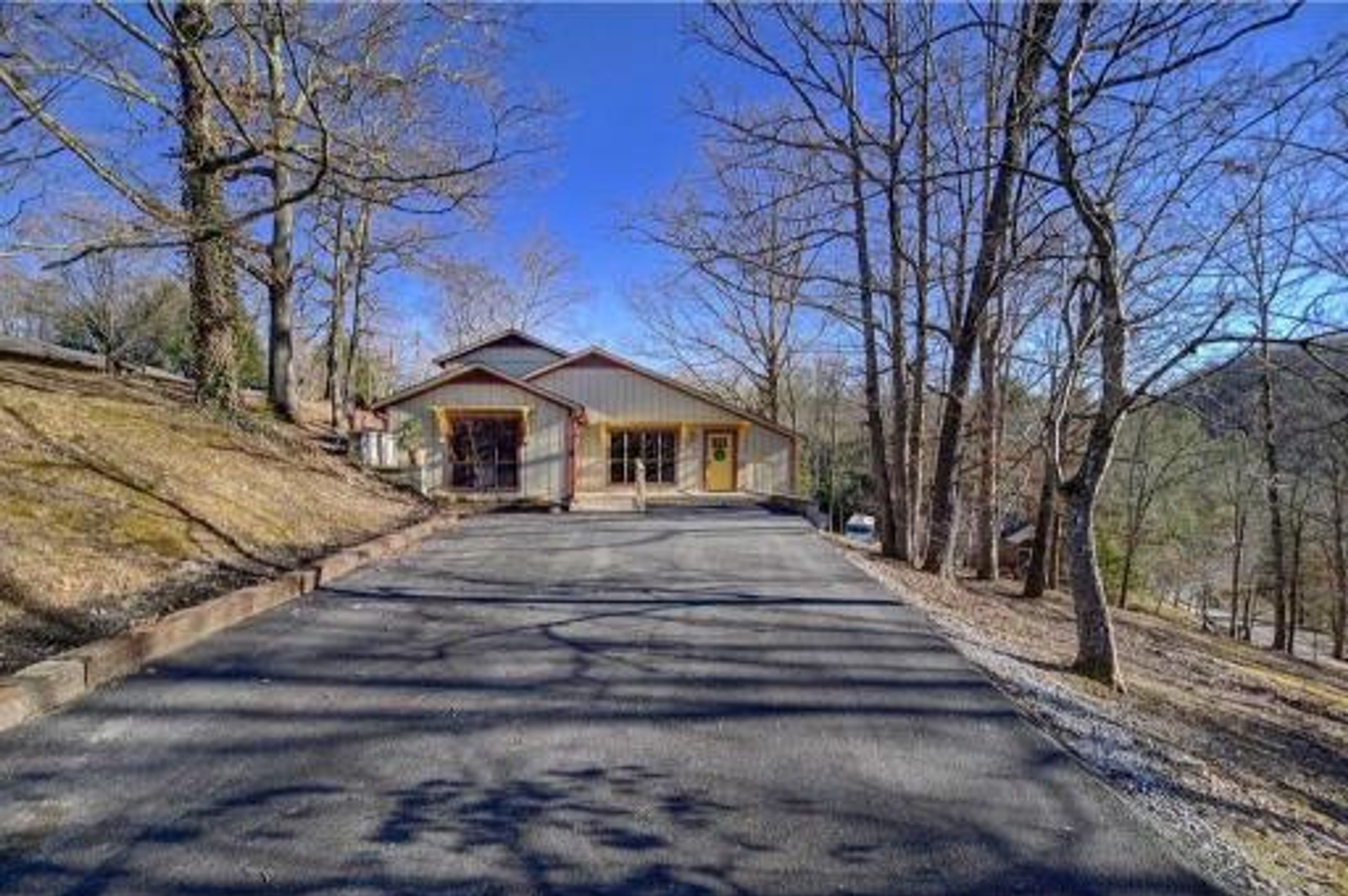 A two-story house with a front entrance, a driveway, and a surrounding wooded area.