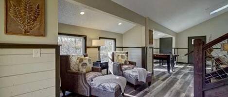 A spacious room with two armchairs, a table, and a staircase.