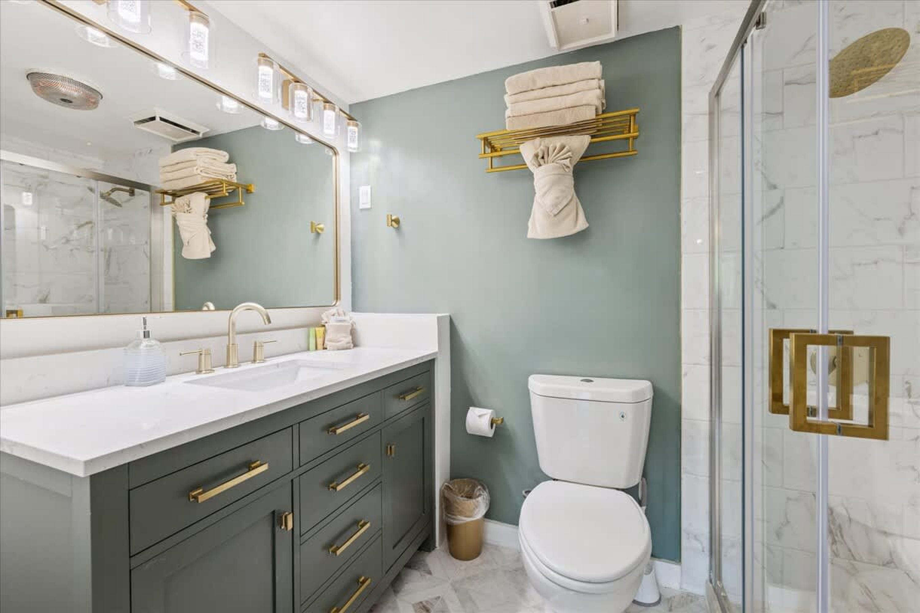 Un baño con un lavamanos blanco, accesorios dorados, un inodoro y una cabina de ducha de vidrio.