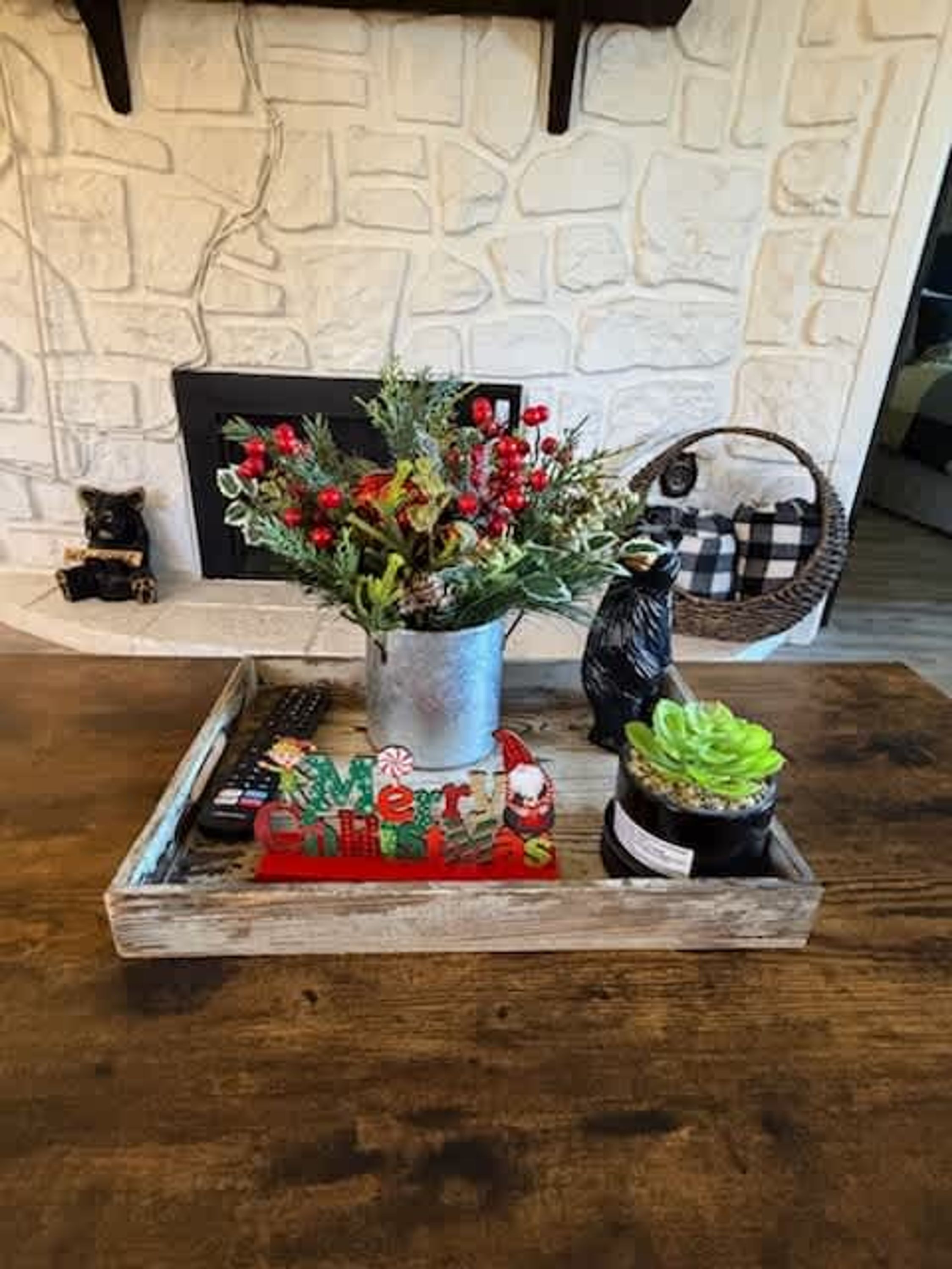 A wooden tray with a Christmas wreath, a small bear figurine, and a checkered basket on a table.