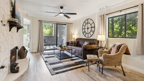 Una sala de estar con chimenea, un reloj grande, un ventilador de techo y vistas al exterior.