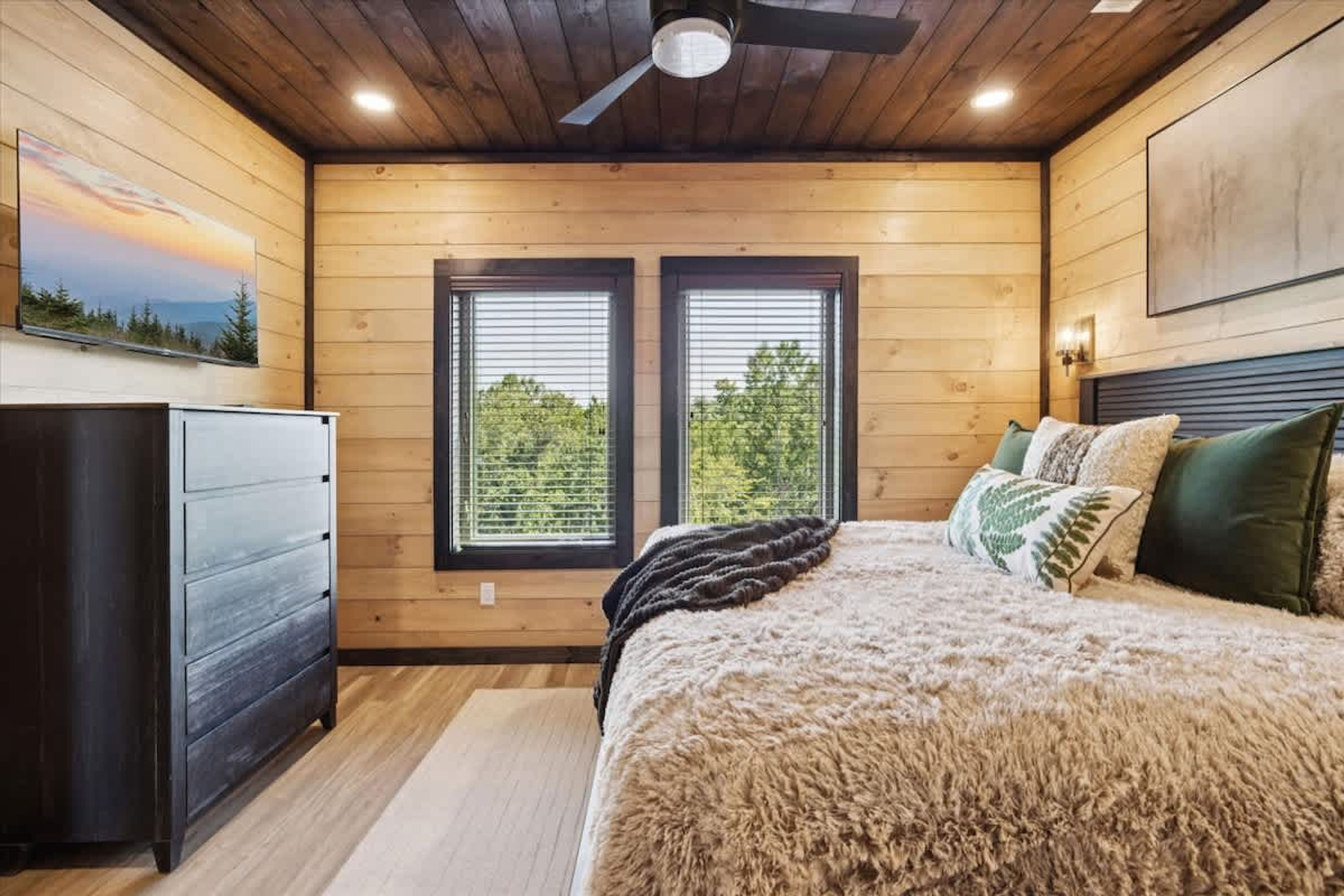 Une chambre à coucher avec un lit, une commode, deux fenêtres et un ventilateur de plafond.