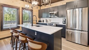 Une cuisine moderne dotée d’un îlot central, de tabourets de bar, d’appareils électroménagers en acier inoxydable et d’un plafond en bois.