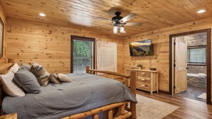 Ein Holzblockhaus-Interieur mit einem Bett, einem Schreibtisch, einem Fernseher und einer Steinwand.