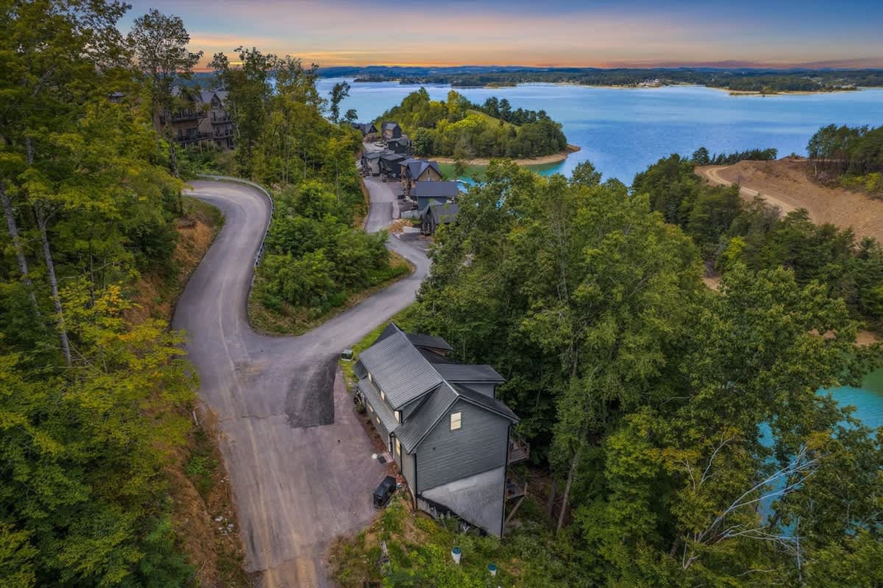 A secluded cabin with a winding road, surrounded by dense forest and a lake.