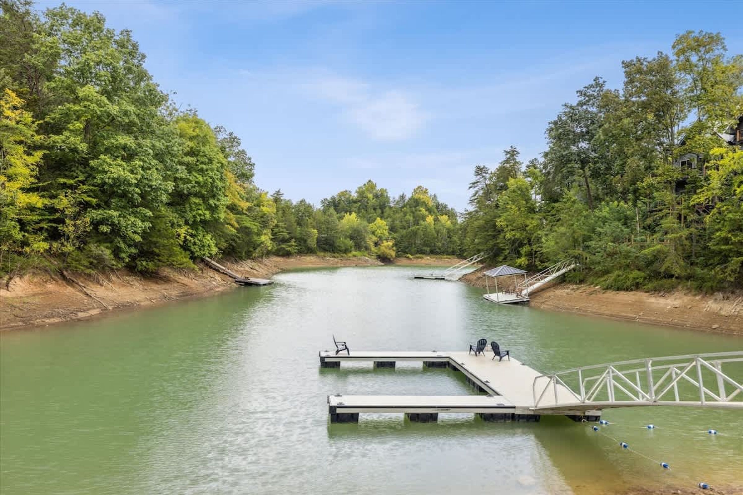 A river with a dock and chairs, surrounded by trees.