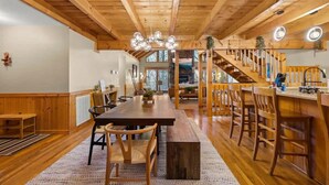 A spacious wooden interior with a long dining table, chairs, a staircase, and a kitchen area. - Round Top Way Cabin by Beyond Expectations (Sevierville)