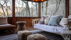 A cozy cabin interior with a wooden bench, a hanging swing, and a view of trees through large windows. - Round Top Way Cabin by Beyond Expectations (Sevierville)