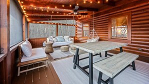 A log cabin interior with a wooden bench, a table, a hanging chair, and string lights. - Round Top Way Cabin by Beyond Expectations (Sevierville)