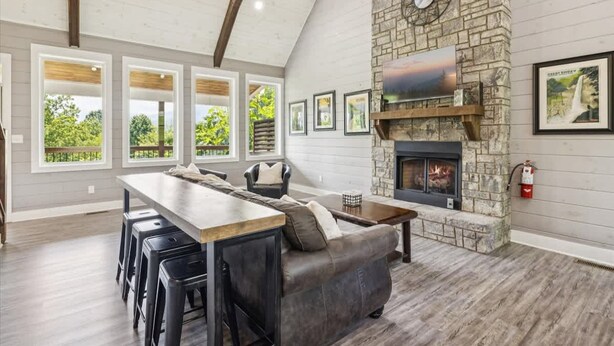 A spacious living area with a stone fireplace, a long dining table, and a sofa. - Mountain View Beauty by Beyond Expectations (Gatlinburg)