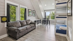 A loft-style bedroom with a bunk bed, a leather sofa, a dining table, and a view of greenery outside. - Mountain View Beauty by Beyond Expectations (Gatlinburg)
