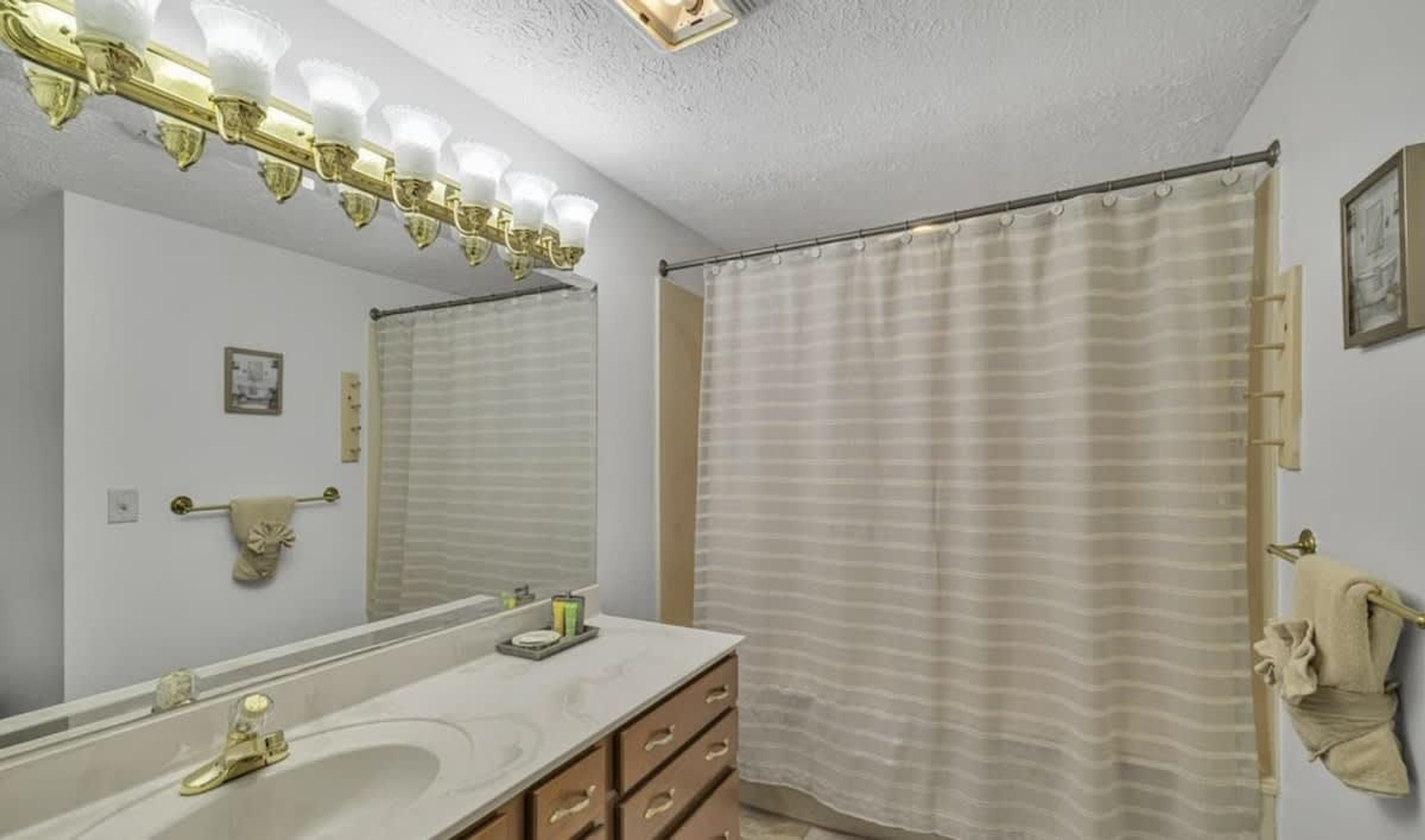 A bathroom with a large mirror, a sink, a vanity with drawers, a shower curtain, and a towel rack.