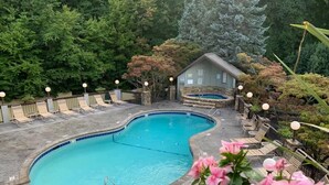 A swimming pool with lounge chairs and a hot tub, surrounded by trees and a stone building. - Misty Mountain Condo by Beyond Expectations With Hot Tub (Gatlinburg)