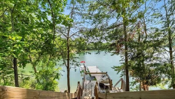 Une terrasse en bois qui mène à un quai surplombant l’eau, le tout entouré d’arbres.