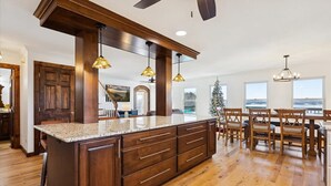 Une cuisine spacieuse dotée d’un grand îlot central, de meubles en bois, de luminaires suspendus et offrant une vue sur l’extérieur.