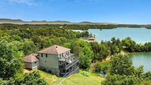 Une maison à deux étages dotée d’un balcon, entourée d’une végétation luxuriante et bordée d’un lac.