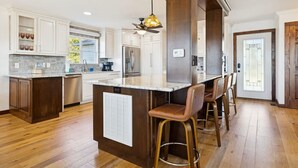 Une cuisine avec des armoires blanches, un îlot en marbre, un plancher en bois et un ventilateur de plafond.