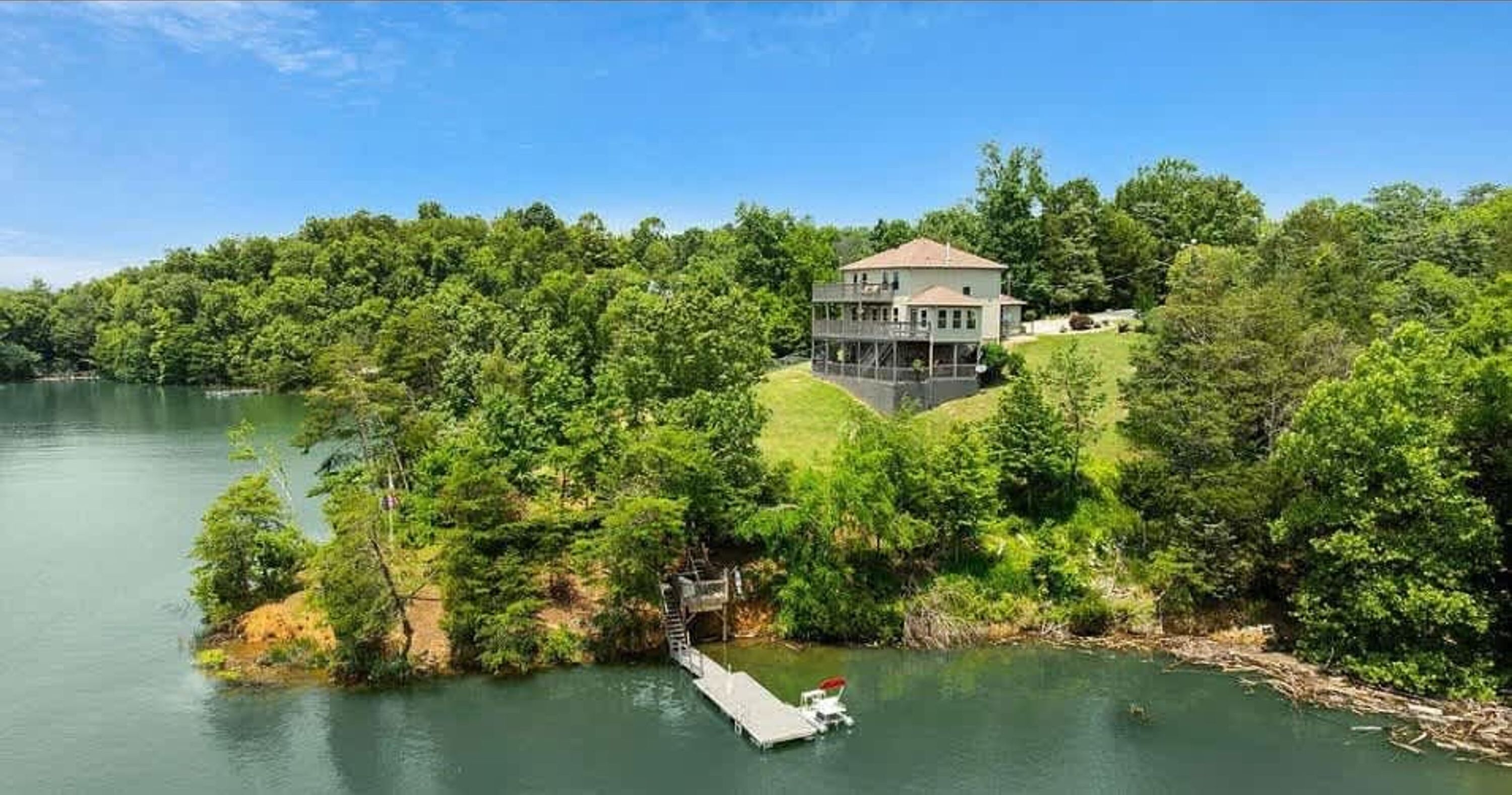 Una casa en una colina con vista a un lago, accesible mediante un muelle.