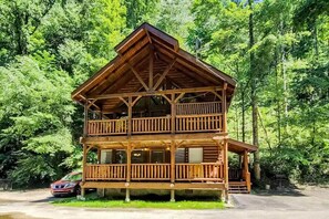 A two-story wooden cabin with balconies, set in a forested area. - Across the Creek Cabin by Beyond Expectations With Hot Tub (Pigeon Forge)