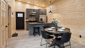 Una cocina moderna con paredes de madera, una isla central, taburetes de bar y una mesa de comedor para cuatro personas.