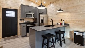 Una cocina moderna con armarios grises, electrodomésticos de acero inoxidable, una isla central con taburetes y paredes de madera.