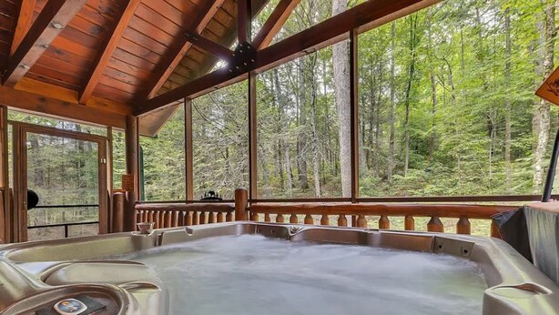 Een hottub in een houten chalet met grote ramen met uitzicht op een bos.