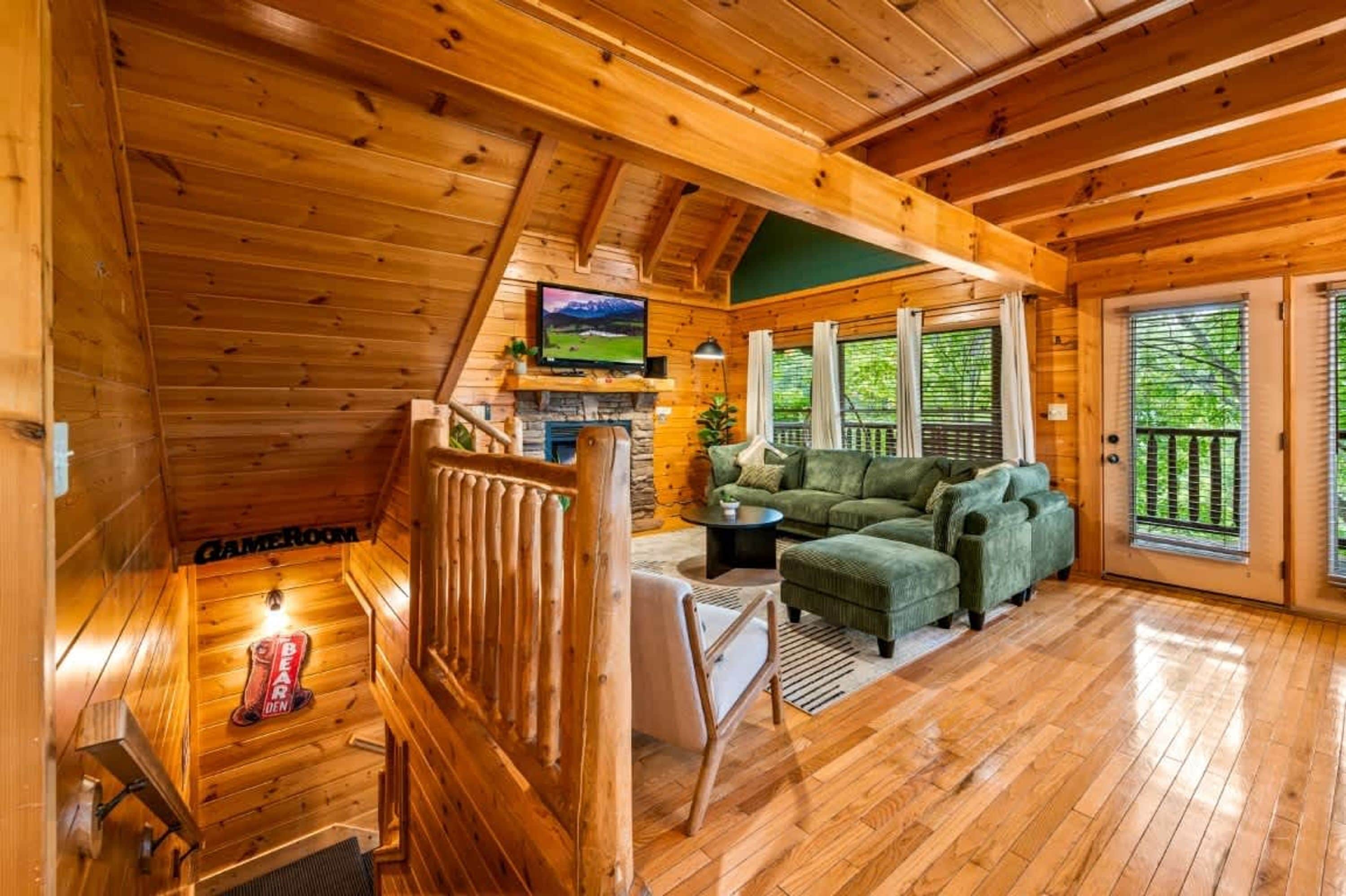 Interior de una cabaña de madera con un dormitorio en altillo, una sala de estar con un sofá verde y una chimenea.