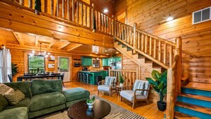 A wooden cabin interior with a staircase, green sofa, dining area, and kitchen. - Smoky Haven Retreat by Beyond Expectations (Sevierville)