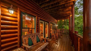A wooden cabin with a porch, benches, and a view of the forest. - Smoky Haven Retreat by Beyond Expectations (Sevierville)