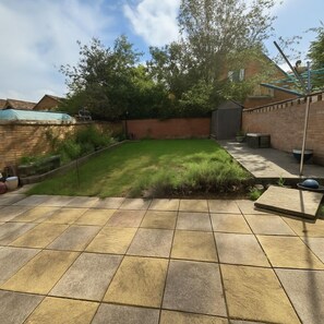 A backyard with a paved patio, a grassy lawn, a brick wall, and a shed. - Clapham Road Apartment (Bedford)
