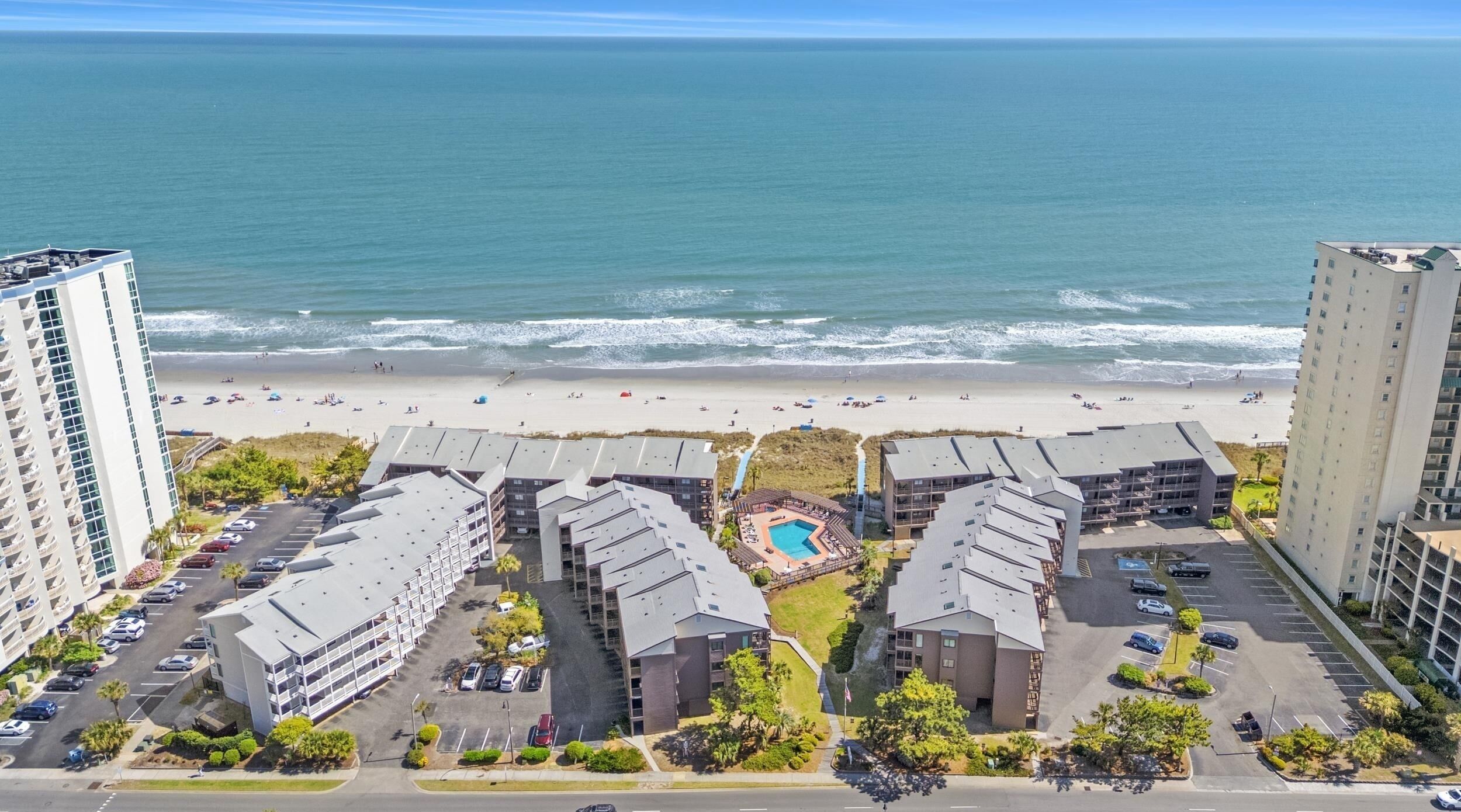 Ein Strandhotel mit mehreren Gebäuden, einem Schwimmbad und einem Strand im Hintergrund.
