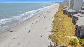 Une plage avec un rivage sablonneux, quelques parasols et des bâtiments en arrière-plan.